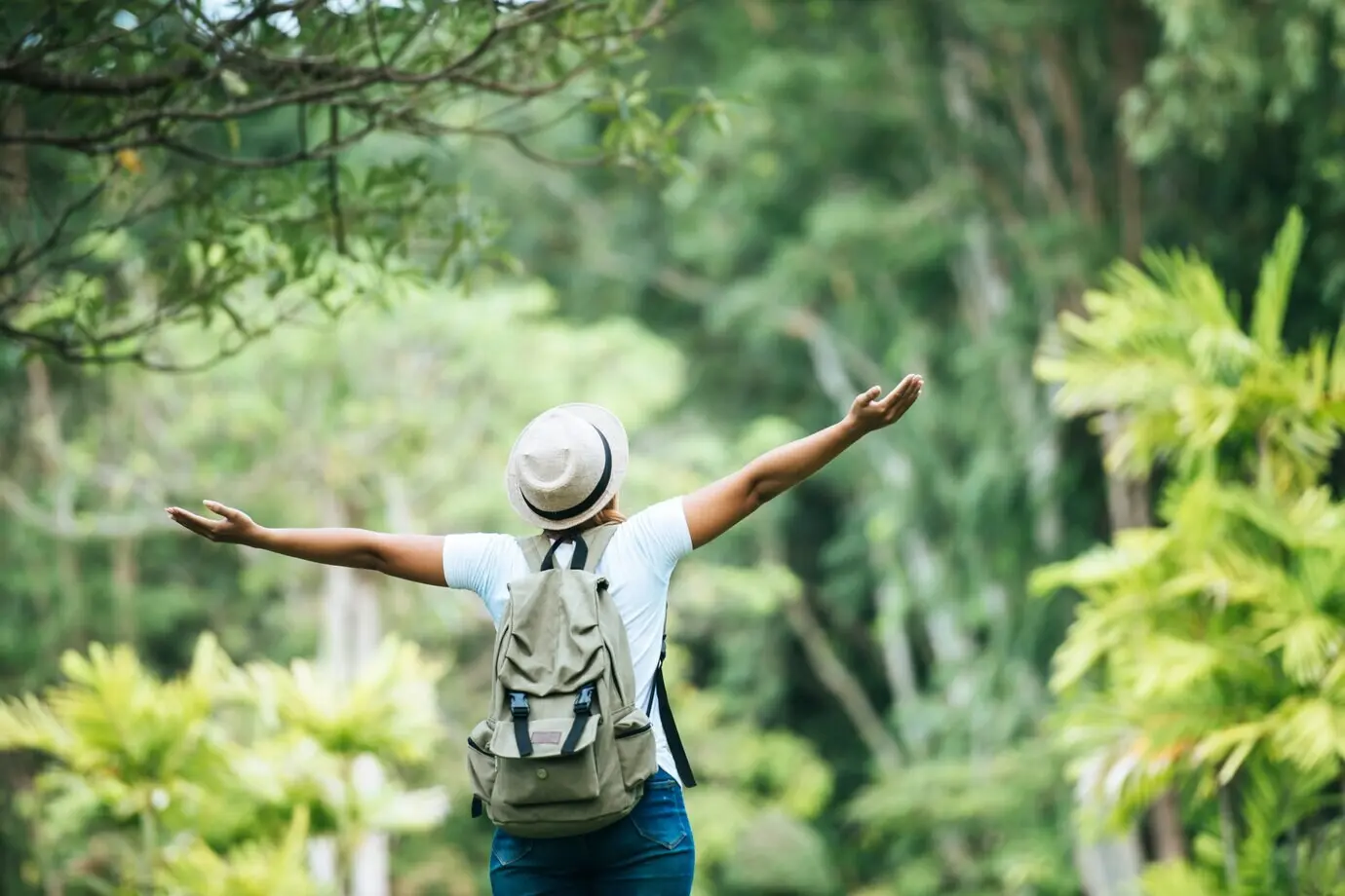 Eine junge glückliche Frau mit Rucksack hebt die Hand und genießt die Natur.